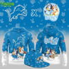 A blue hoodie featuring Bluey and Bingo from the children's show "Bluey" alongside the Detroit Lions logo. The hoodie has a playful design with characters in sports outfits, engaging in activities like football, with paw prints and other cute symbols in the background.