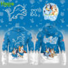 A close-up view of a blue hoodie with a larger design showing Bluey and Bingo, from the show "Bluey," paired with the Detroit Lions logo. The hoodie features a bold graphic with the characters running in sports outfits.