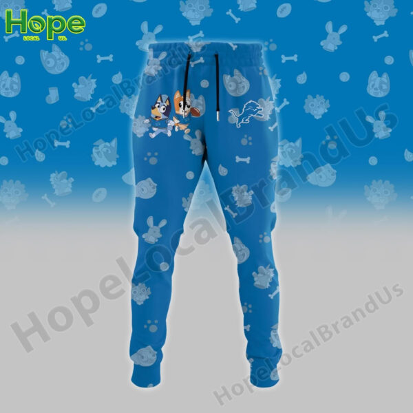 A pair of blue sweatpants featuring Bluey and Bingo from the animated show "Bluey," alongside the Detroit Lions logo. The pants have a vibrant design with paw prints and fun character illustrations.